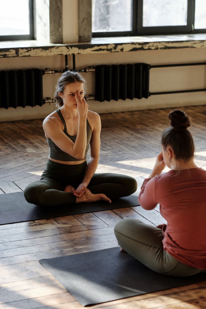 About Two women meditating and practicing yoga indoors, focusing on inner peace and wellness.