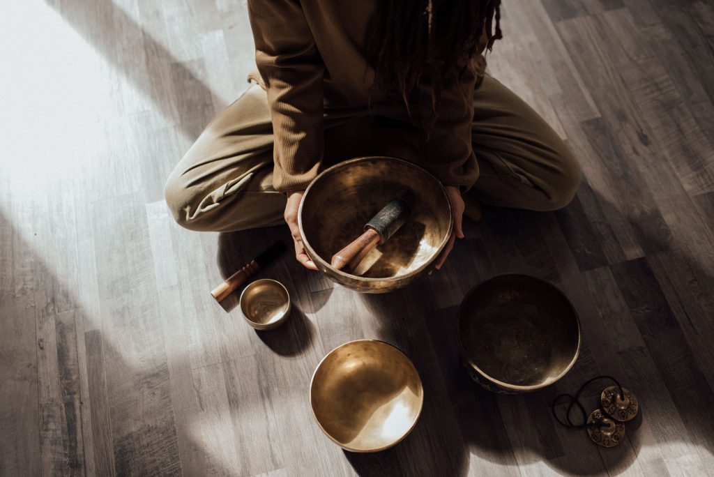Services A woman engaging in a meditative sound bath using Tibetan singing bowls on a wooden floor.